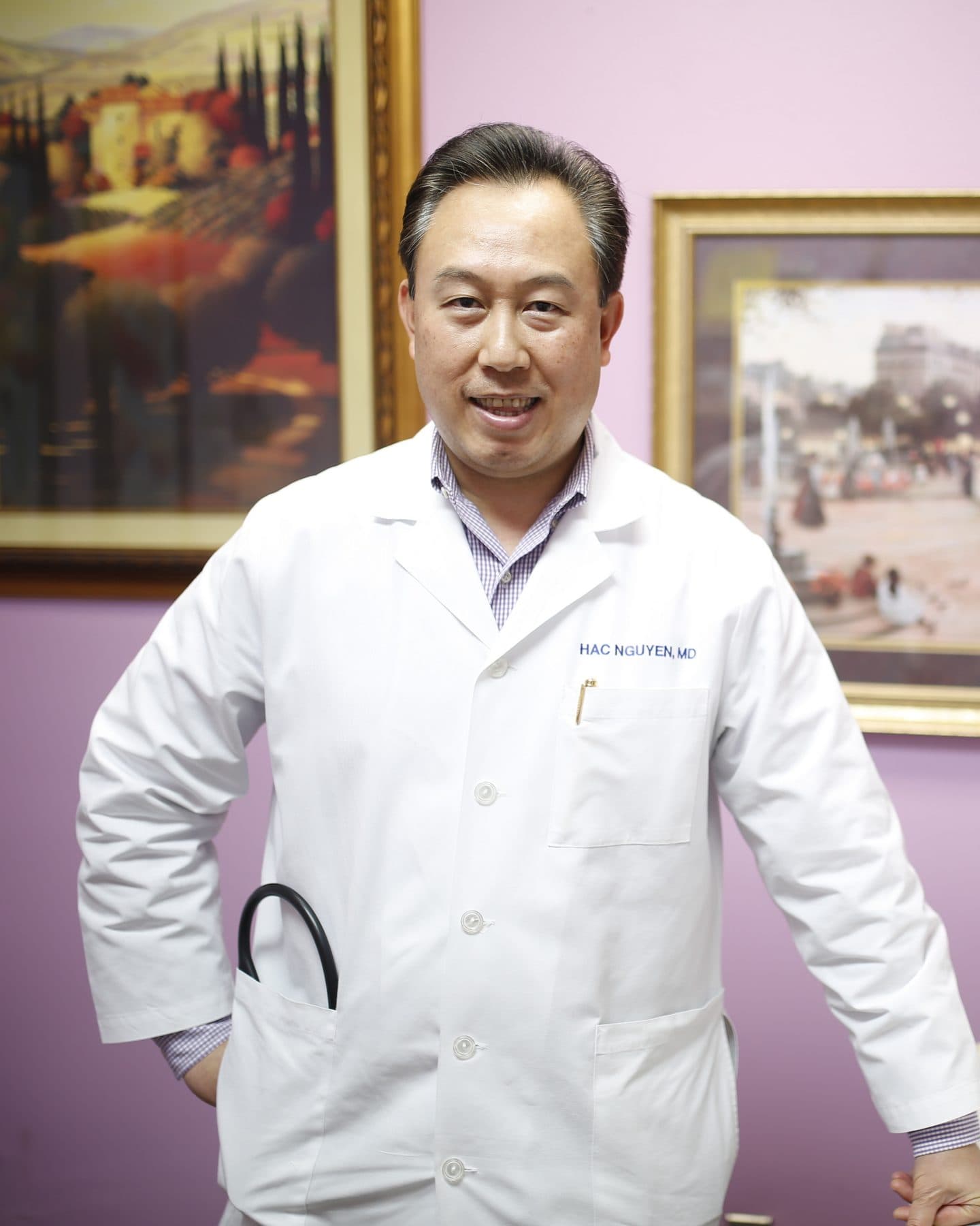 Dr. Hac Nguyen in his exam room in a white coat embroidered with his name